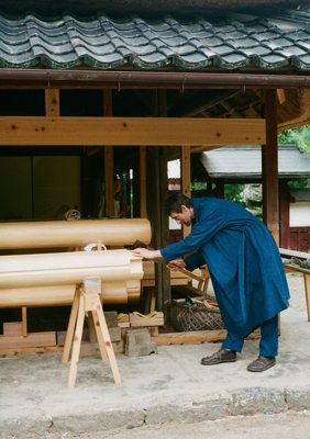 Sébastien cutting lumber for a sheep hut under construction, Organic cotton broadcloth ryukyu indigo-dyed haori coat and European stripe combination wrapped pants